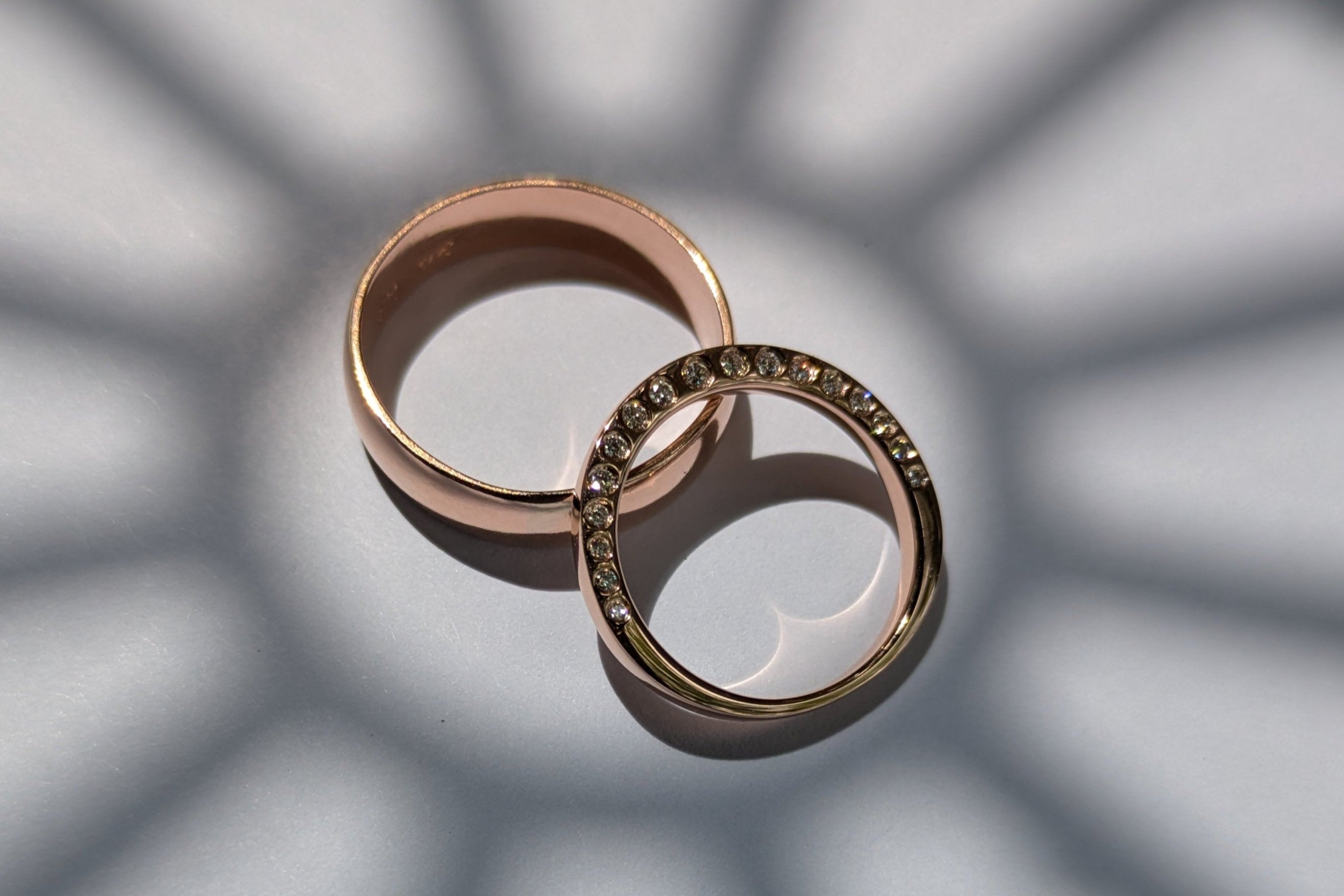 Two rose gold rings on a surface with geometric shadow patterns