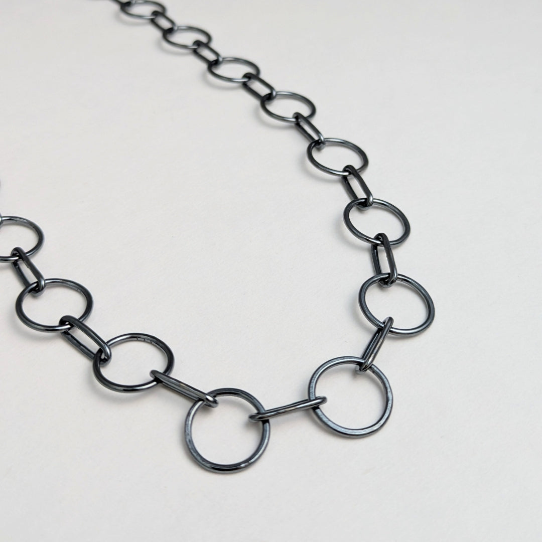 A close-up image of a sterling silver circle chain necklace with a hand-fabricated S-clasp.