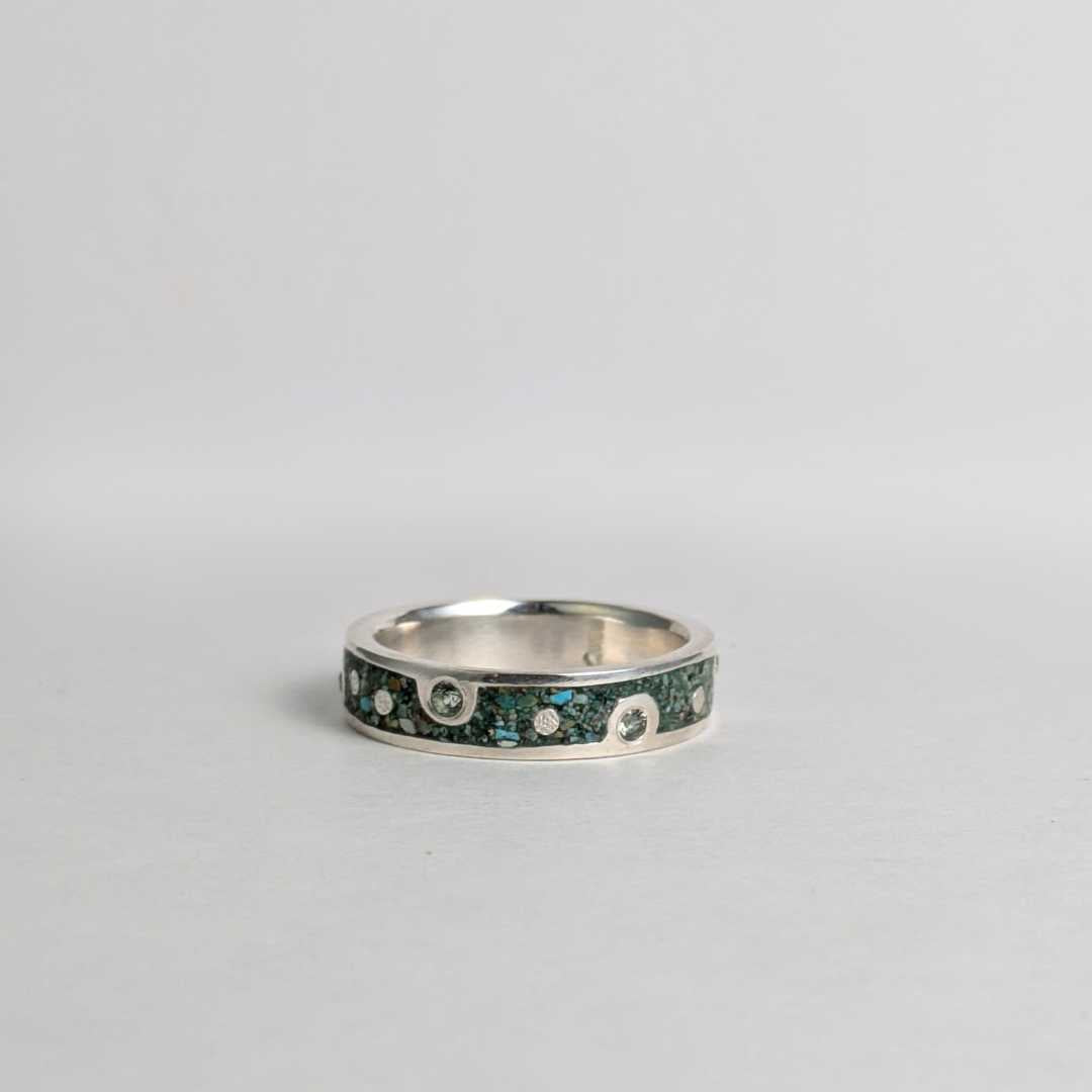 Silver ring with embedded green sapphires on a gray background