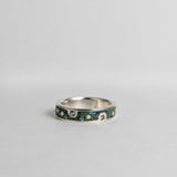 Silver ring with embedded green sapphires on a gray background