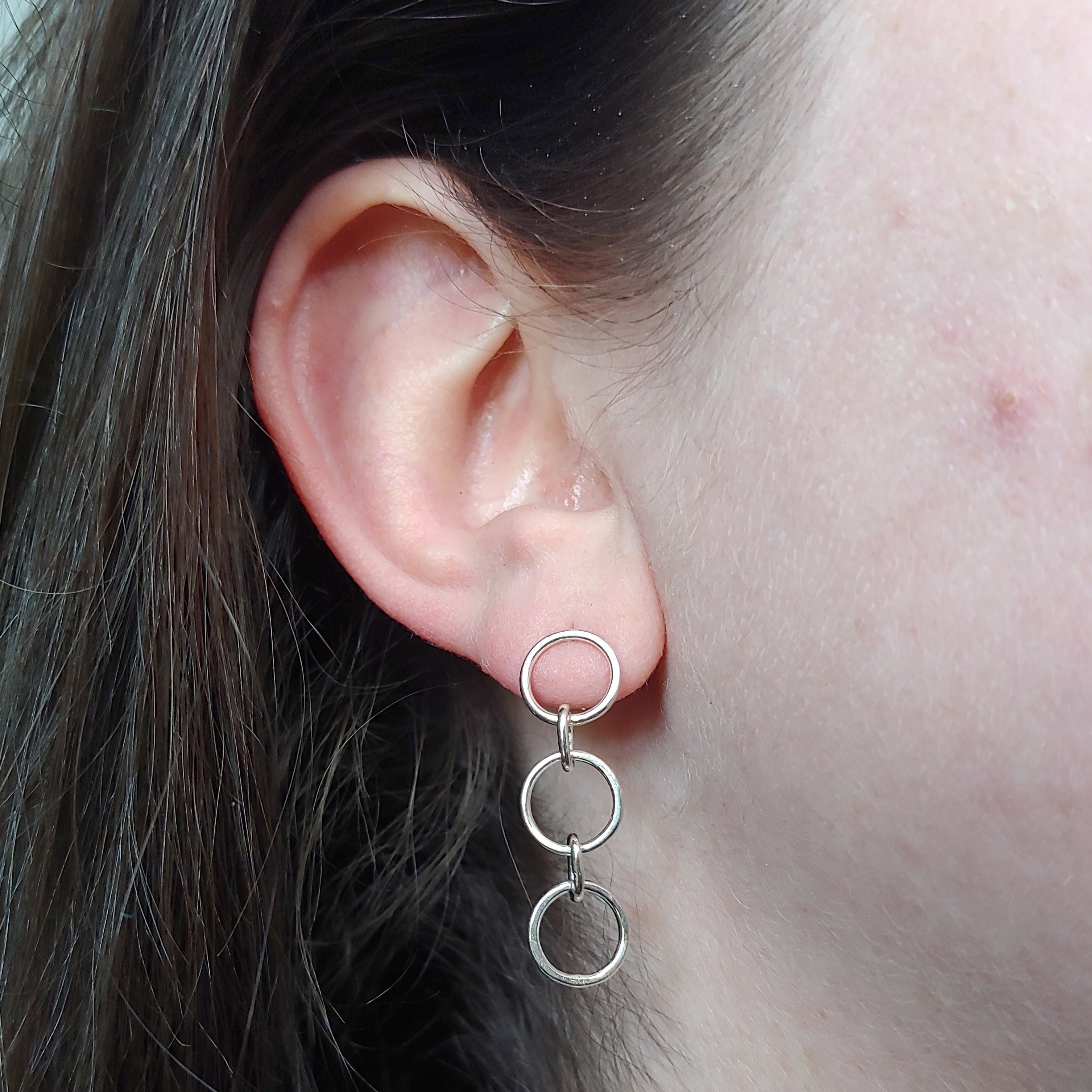 A close-up image of a person's ear wearing a mini chain link stud earring.